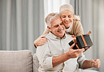 Happy couple, together and love with gift at home in embrace for birthday, anniversary or event. Mature, man and woman in living room, celebration and bond in happiness with hug, smile and special