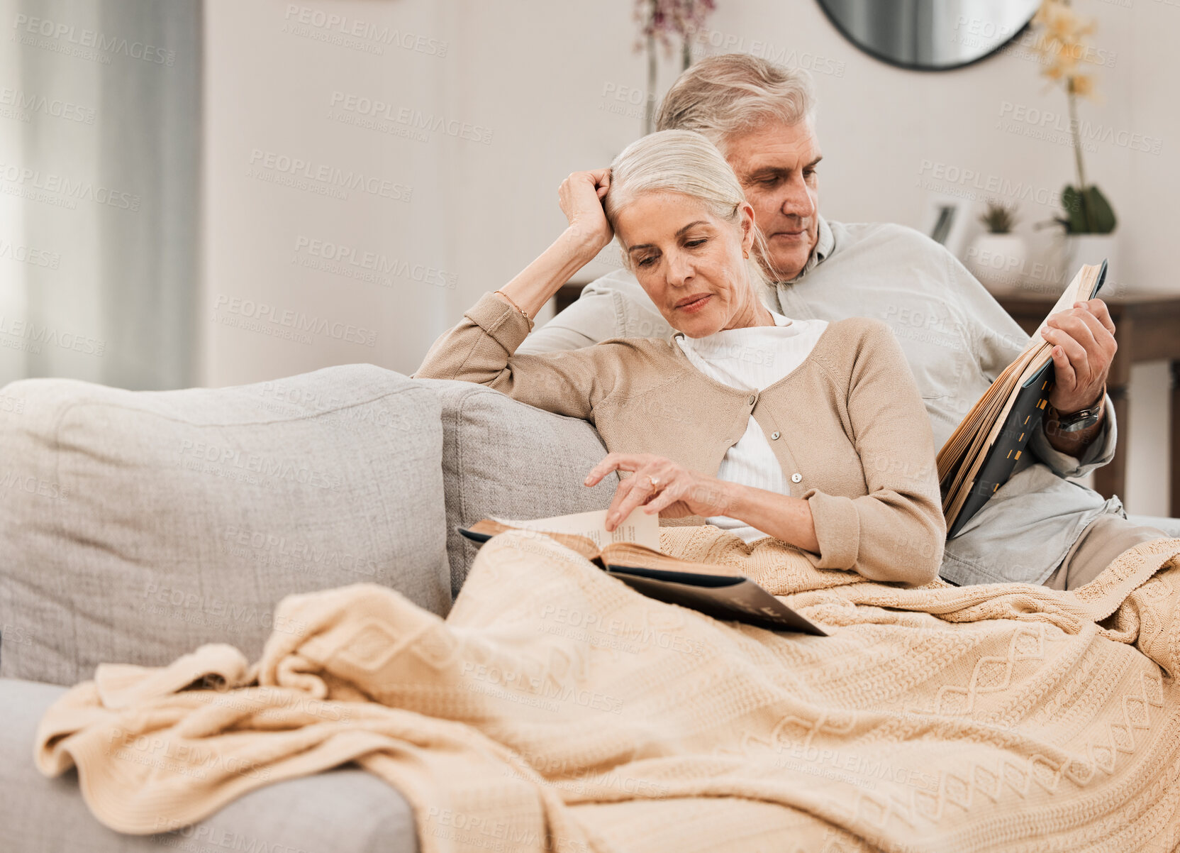 Buy stock photo Old couple on couch, reading book and relax together at home, retirement and wellness with love and comfort. Trust, care and support in marriage, share hobby with partner for knowledge and story