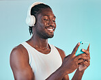 Headphones, cellphone and black man in a studio networking and listening to music, playlist or album. Happy, smile and African male model scroll on internet with phone and song by blue background.