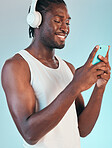 Smartphone, headphones and black man listening to music, smile with audio streaming and chat isolated on blue background. Happiness, sound and mobile app, podcast or radio with connectivity in studio