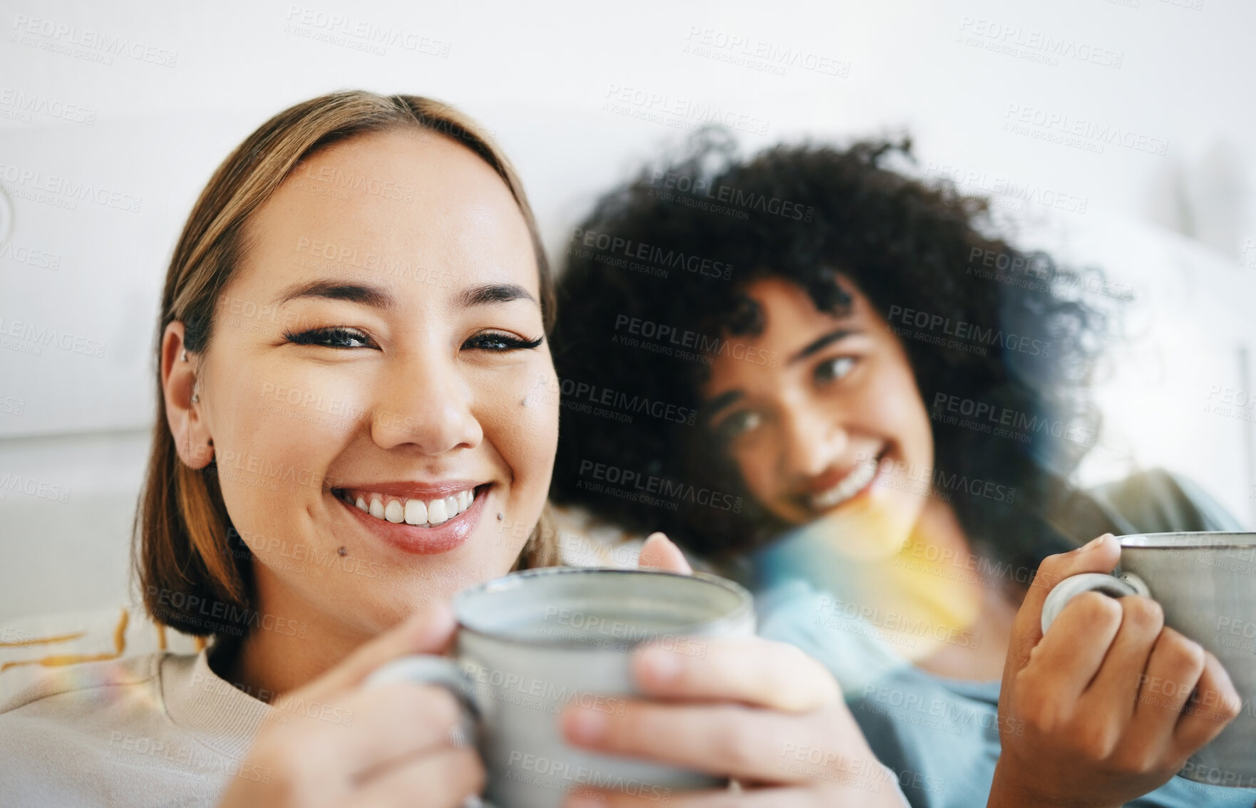 Buy stock photo Coffee, smile and portrait of lesbian couple on bed in conversation for bond and relax together. Happy, rest and interracial lgbtq women laughing, talking and drinking latte in bedroom of apartment.