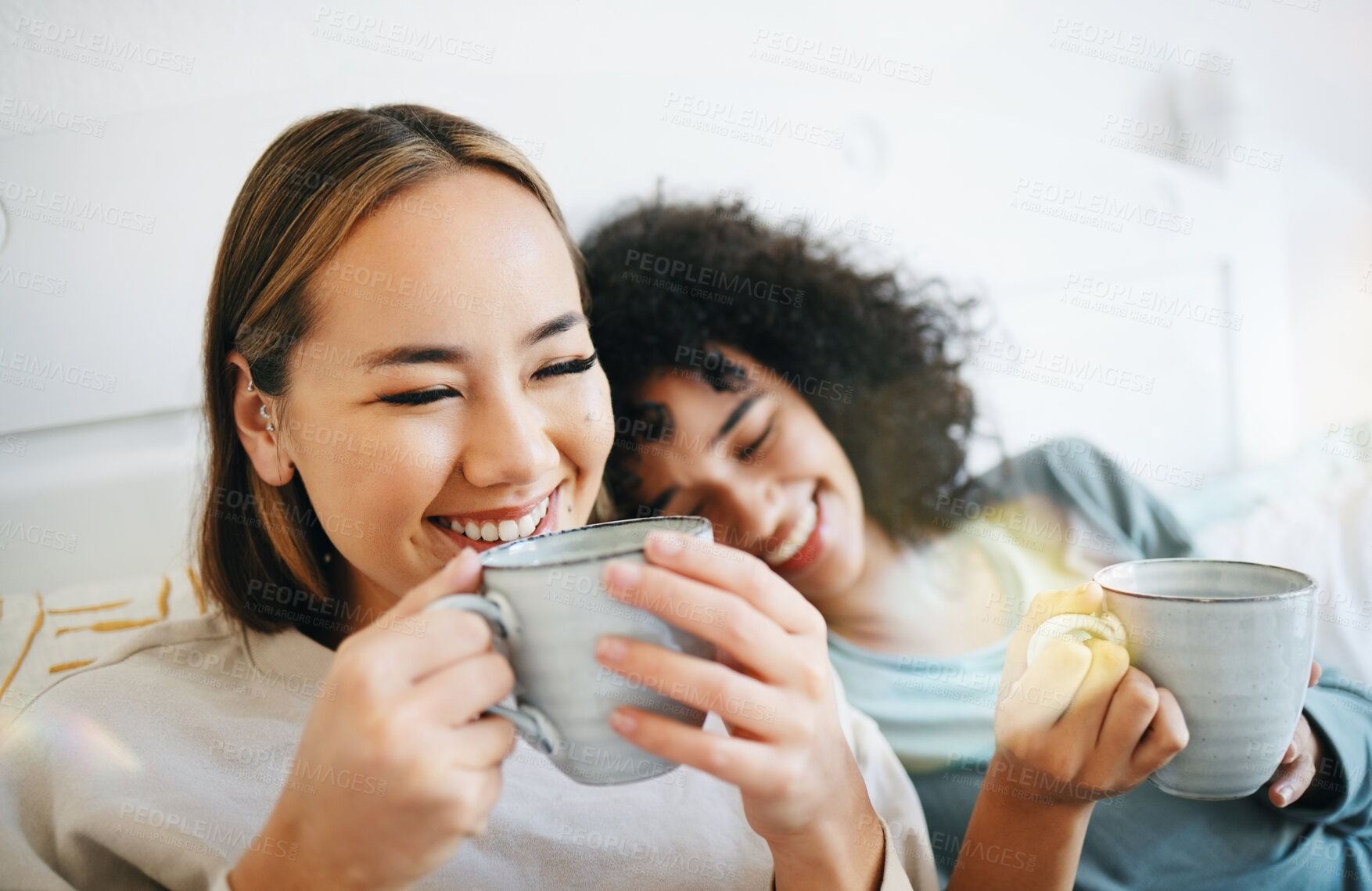 Buy stock photo Coffee, laugh and lesbian couple on bed in conversation for bonding and relaxing together. Happy, rest and young interracial lgbtq women talking and drinking latte in bedroom of modern apartment.