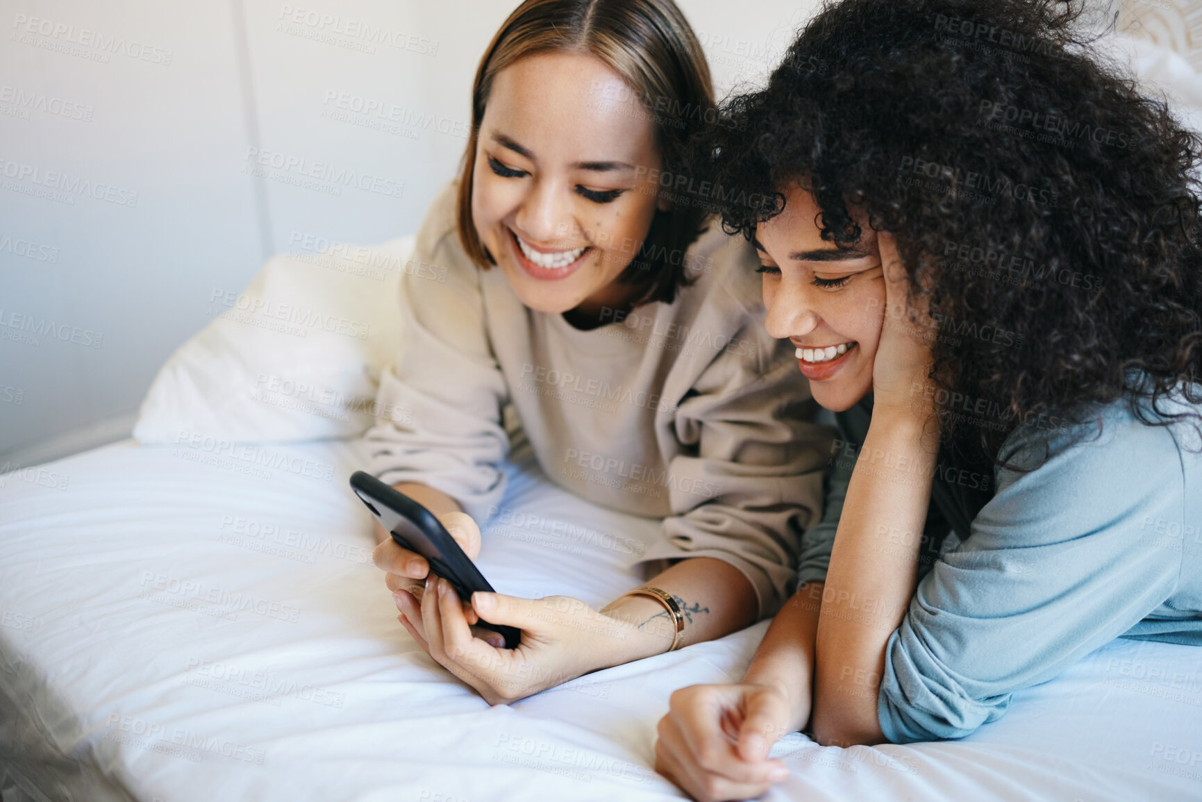 Buy stock photo Phone, relax and young lesbian couple on a bed networking on social media, mobile app or the internet. Happy, technology and interracial lgbtq women scroll on cellphone in bedroom at modern apartment
