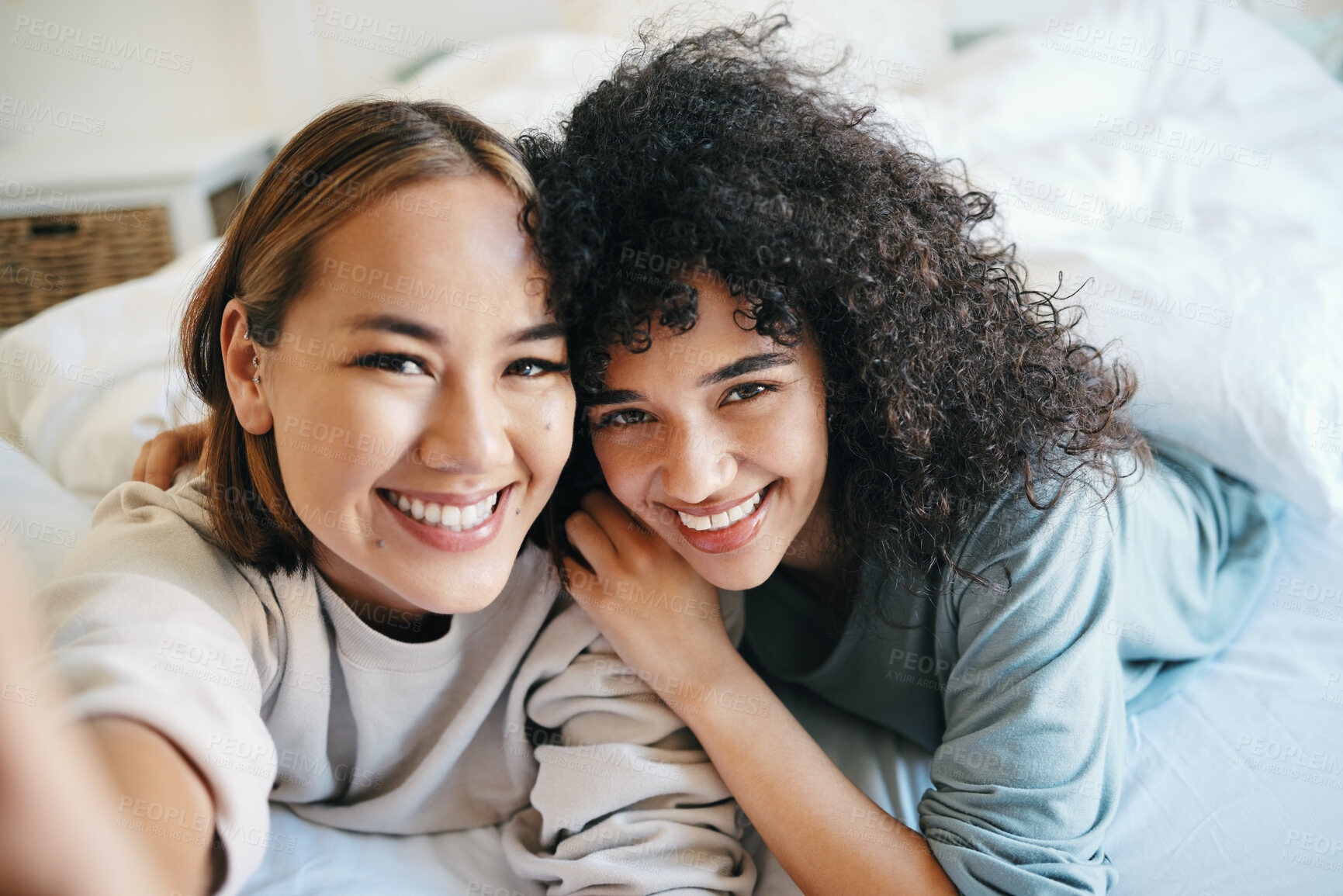 Buy stock photo Smile, selfie and portrait of lesbian couple on bed for bonding, resting or relaxing together. Happy, love and young interracial lgbtq women taking picture in the bedroom of modern apartment or home.