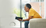 Senior man, reading and thinking with book on sofa in home living room learning knowledge, information or ideas. Elderly, person and relax in retirement with novel, books or fiction with mockup space