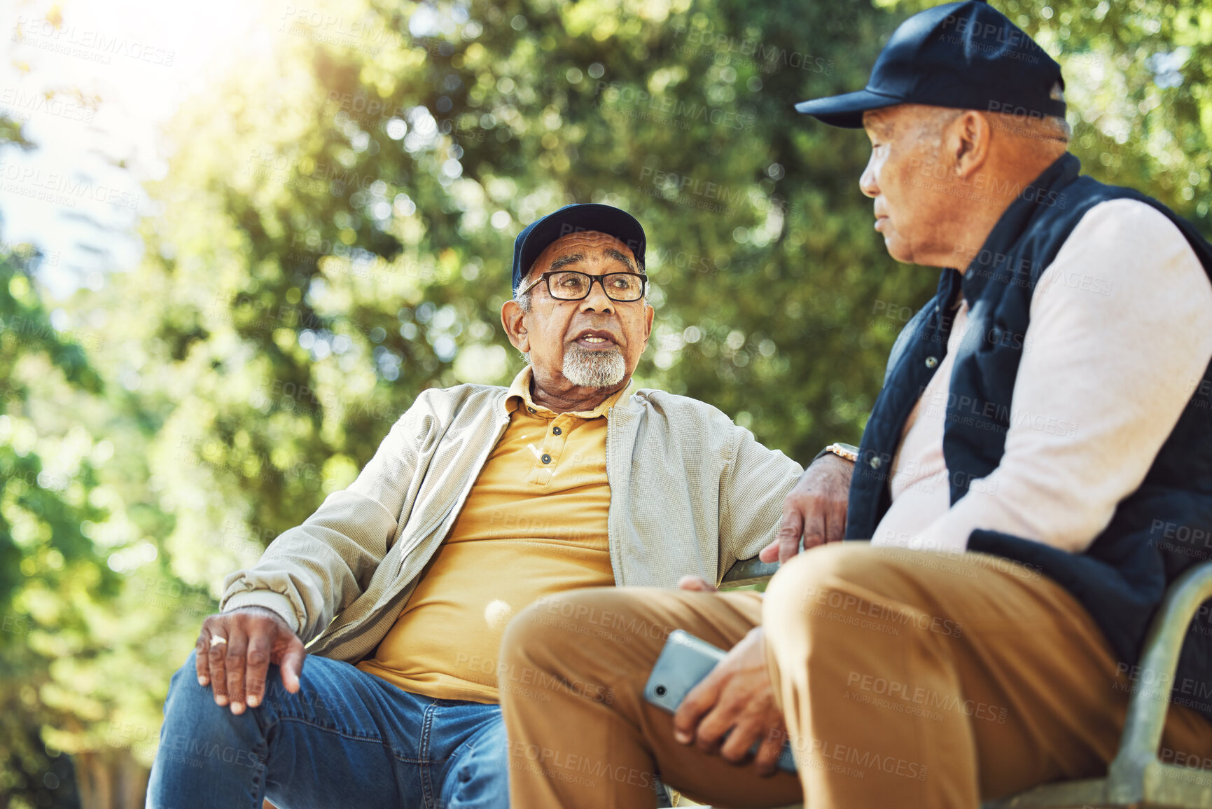 Buy stock photo Elderly friends, men and relax at park bench, talk and bonding outdoor with phone. Senior people sitting together in garden, communication and serious conversation in nature for retirement in spring