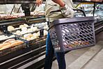 Hands, basket and person grocery shopping in bakery, store and supermarket for food. Groceries, market and customer in retail shop for choice of product, sales deal and discount on bread or dessert