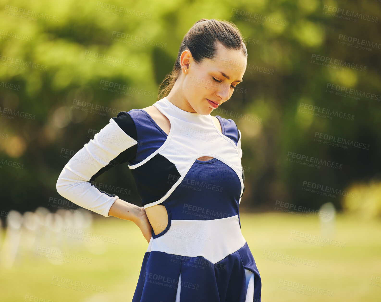 Buy stock photo Cheerleader, fitness injury and back pain from sport, training and cheer exercise on a grass field. Health, accident and woman muscle bruise outdoor with emergency and workout challenge for wellness