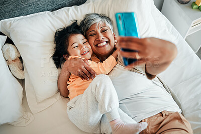 Buy stock photo Selfie, smile and grandmother with child on bed bonding, relax and love for happy family with care. Photography, technology and senior woman with little girl in bedroom on video call together in home