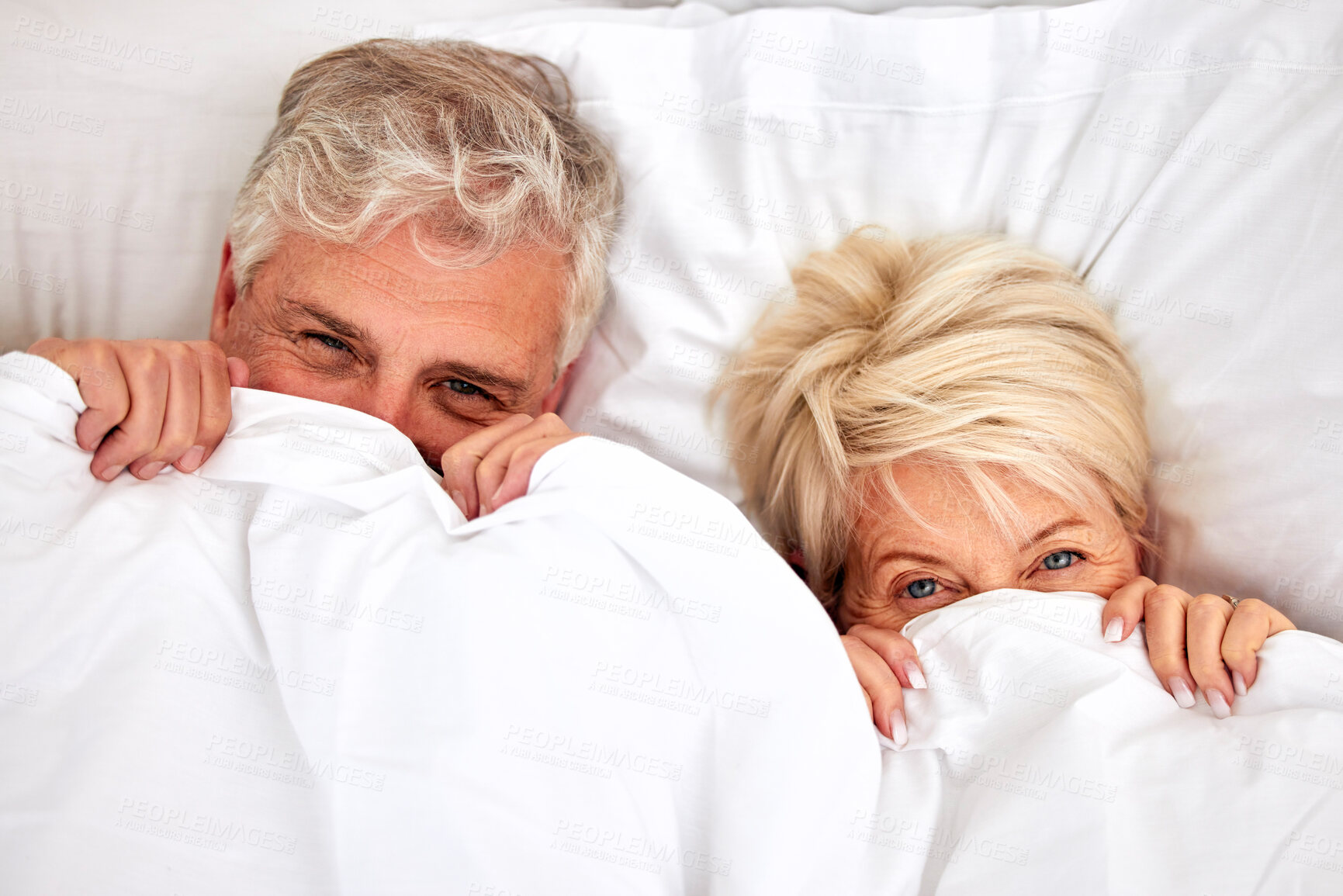 Buy stock photo Hiding, portrait and a senior couple in bed for comfort, sleep or love in retirement. Shy, intimate and an elderly man and woman in the bedroom of a house with a blanket covering head in marriage