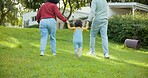 Family, walking and parents support a child in a backyard bonding by a home or house for care or love for a holiday. Outdoor, mother and father enjoying quality time and playing with kid in back view