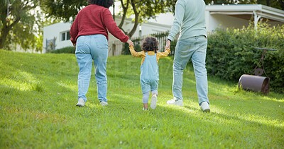 Family, walking and parents support a child in a backyard bonding by a home or house for care or love for a holiday. Outdoor, mother and father enjoying quality time and playing with kid in back view
