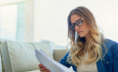 Buy stock photo Shot of an attractive young woman reading paperwork while working at home