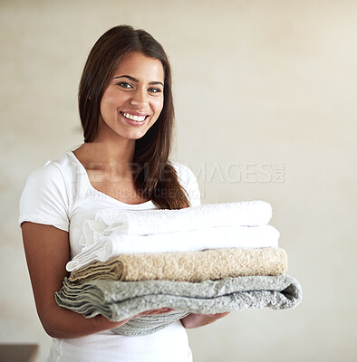 Buy stock photo Portrait of a happy young woman holding a pile of clean folded towels