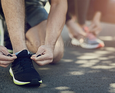 Buy stock photo Cropped shot of two unrecognizable people tying their laces before a run