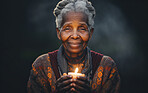Senior African American woman praying with candle in hand. Studio backdrop. Religion concept.