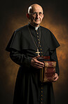 Studio portrait of senior catholic priest in traditional attire holding bible. Religion concept.