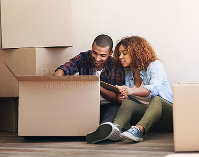 Buy stock photo Shot of a young couple unpacking a box together while sitting on the floor of their new home