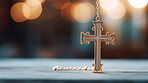 Close up of small cross hanging from chain on table. Copy space. Religion and faith concept.