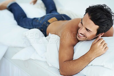Buy stock photo Shot of a happy-looking young man lying on his stomach in bed