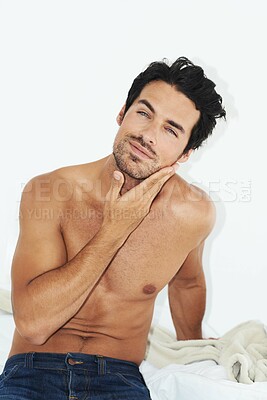 Buy stock photo Shot of a handsome bare-chested man sitting on his bed and rubbing his chin