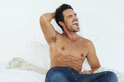 Buy stock photo Shot of a bare-chested young man sitting on his bed and yawning