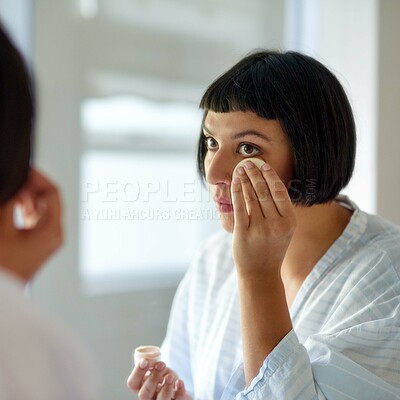 Buy stock photo Shot of a young woman in a bathrobe applying foundation in her bathroom mirror in the morning