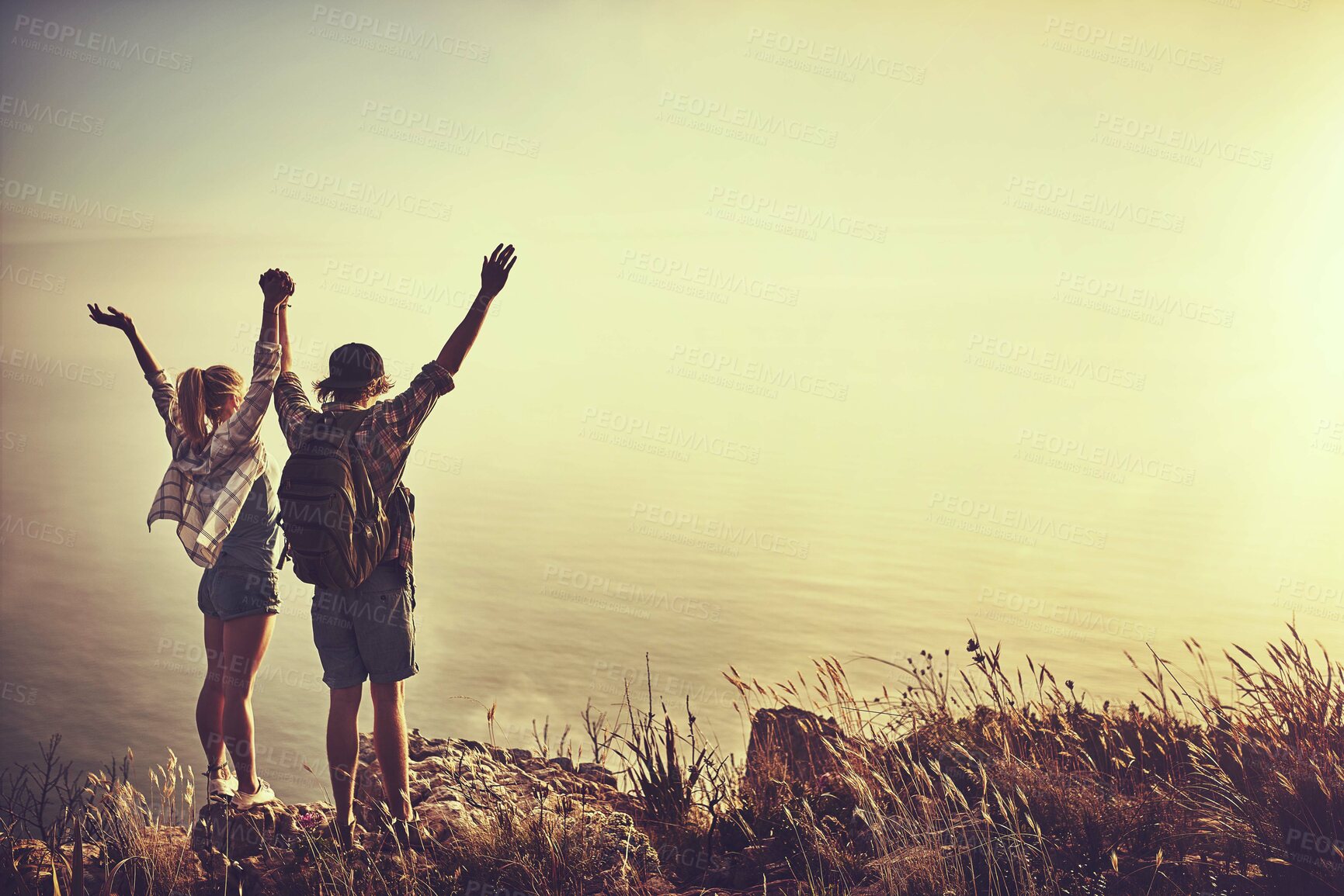 Buy stock photo Rearview shot of an unidentifiable young couple admiring the view from a mountain peak together