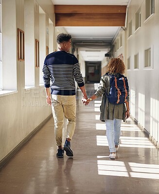 Buy stock photo Rearview shot of an affectionate young couple walking hand in hand through their university corridor
