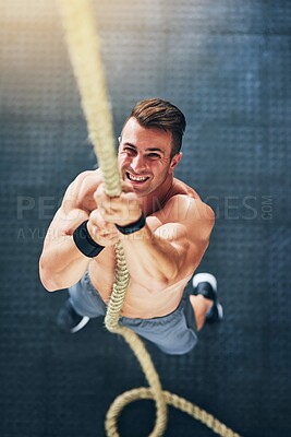 Buy stock photo Shot of a muscular young man climbing a rope at the gym