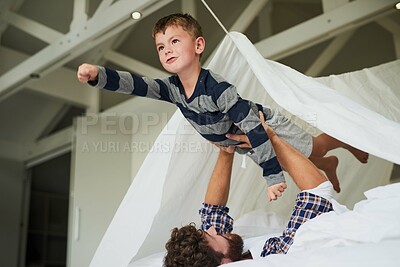 Buy stock photo Cropped shot of a young man holding his son up like a superhero while playing on the bed