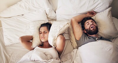 Buy stock photo Shot of a young woman covering her ears with a pillow while her husband snores in bed