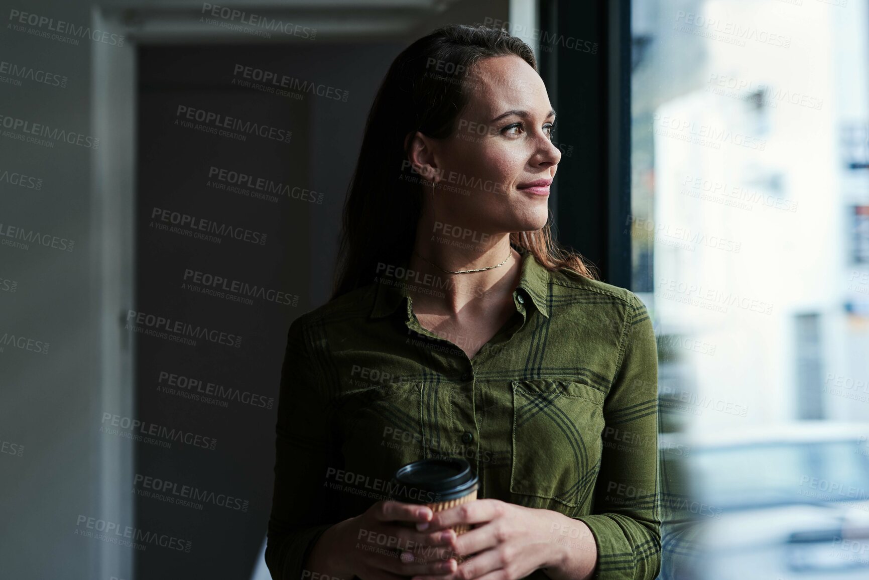 Buy stock photo Shot of an attractive young businesswoman drinking coffee and looking out the window of her office