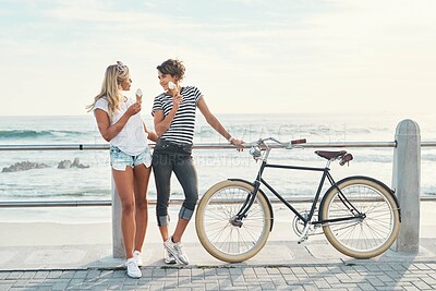 Buy stock photo Shot of two friends eating ice cream while standing on the promenade with a bicycle