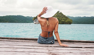 Buy stock photo Travel, hat and back of woman on an island to relax while on tropical summer vacation or holiday. Adventure, outdoor and female person sitting on wood pier by ocean water on weekend trip in paradise.