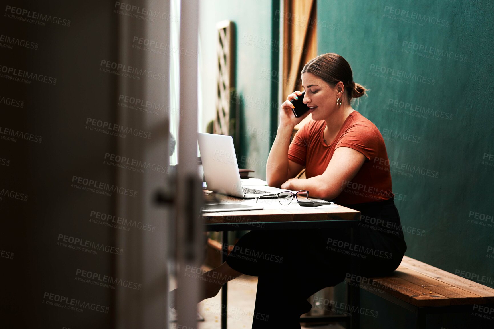 Buy stock photo Cropped shot of an attractive young businesswoman sitting alone and using her cellphone while using her laptop