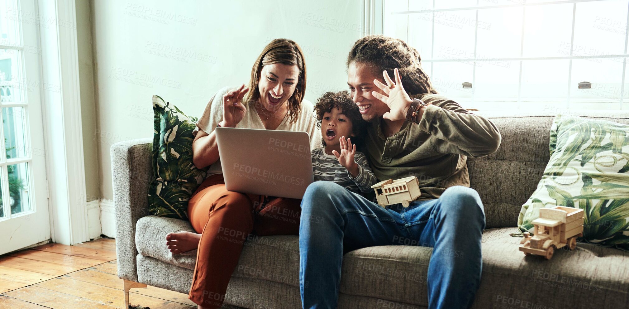 Buy stock photo Shot of a cheerful young couple and their son having a video call to relatives on a laptop while being seated on a sofa at home