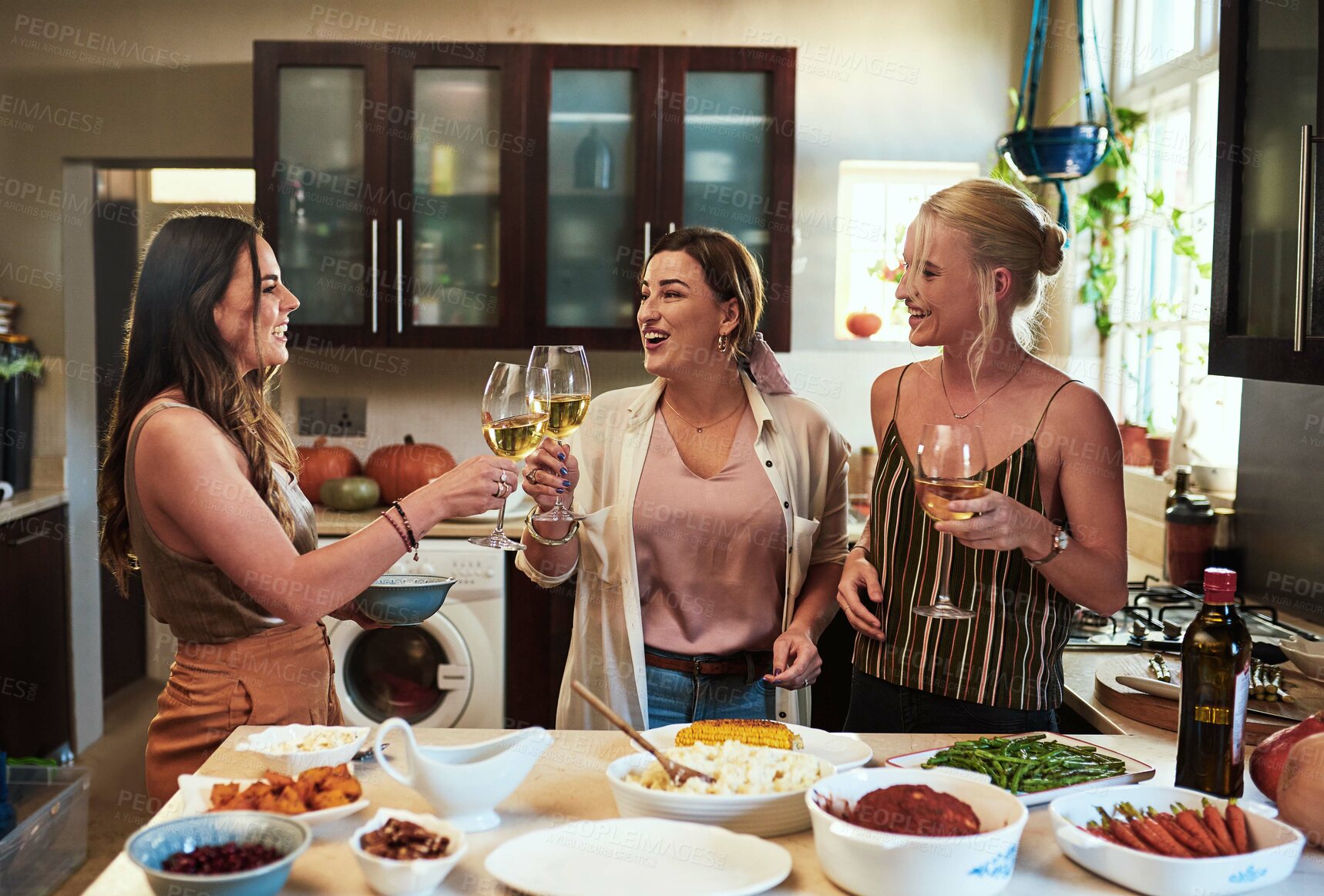 Buy stock photo Cropped shot of a group of cheerful young friends having a celebratory toast with drinks while standing in the kitchen preparing food at home