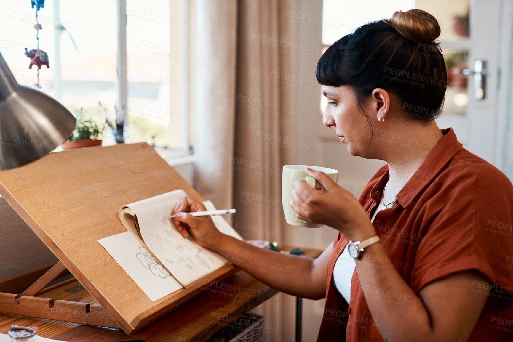 Buy stock photo Shot of a young woman drinking coffee while sketching at home