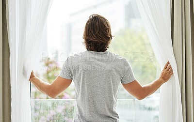 Buy stock photo Shot of a young man opening the curtains in the morning to a bright,sunny day.