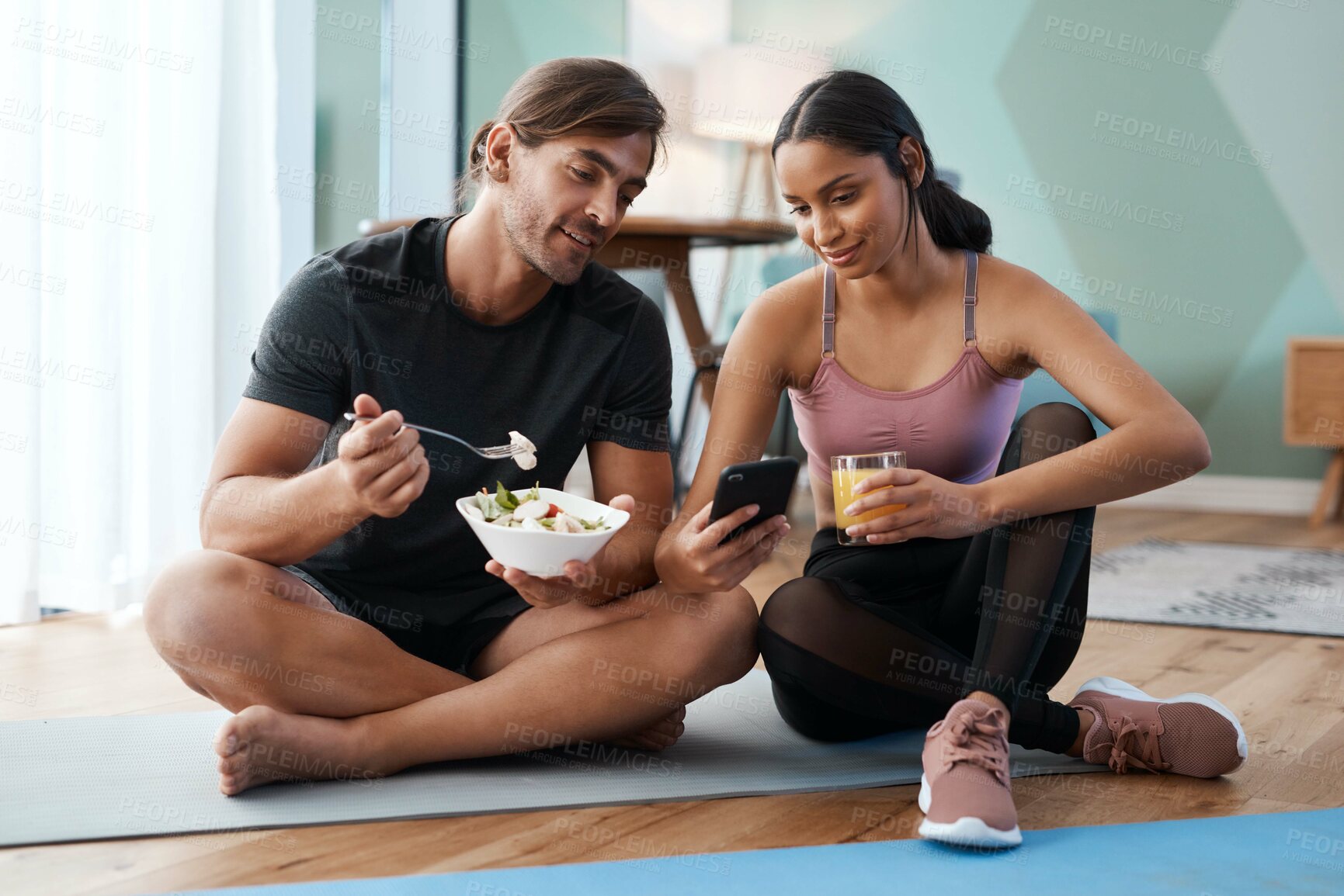 Buy stock photo Full length shot of an athletic young couple enjoying some healthy snacks after their workout at home