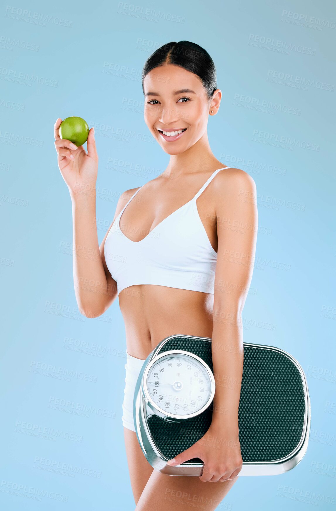 Buy stock photo Studio portrait of a young woman holding an apple and scale while posing against a blue background