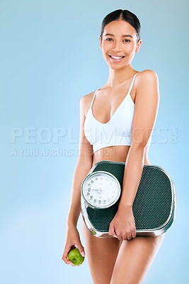 Buy stock photo Studio portrait of a young woman holding an apple and scale while posing against a blue background