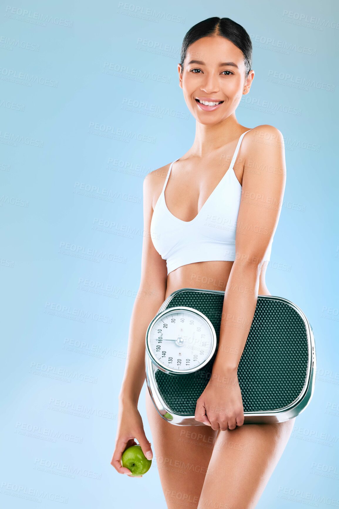 Buy stock photo Studio portrait of a young woman holding an apple and scale while posing against a blue background