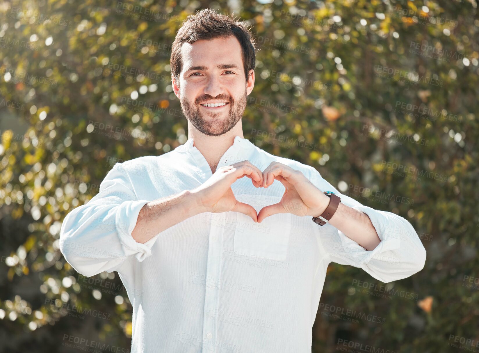 Buy stock photo Cropped portrait of a handsome young man making a heart shape with his hands outdoors