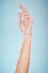 Water drops, hand and closeup with cleaning, shower and morning dermatology in studio. Blue background, person arm and splash for wellness, washing and skin glow with self care and hygiene safety