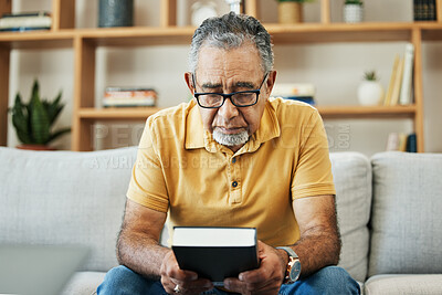 Buy stock photo Mature, man and bible by thinking in home, alone and sadness of memory in living room of thoughts. Elderly, person or grandfather on sofa with hand, holding and book for religion, church or practice