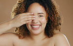 Portrait, funny or happy woman with natural beauty dermatology for wellness in studio with smile. Hand, eye cover or biracial female person laughing with skincare, pride or glow on brown background