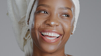 Buy stock photo Face, beauty and lotion with a happy black woman in studio on a gray background for natural wellness. Skincare, smile and cream with a happy young model closeup to apply treatment to her skin