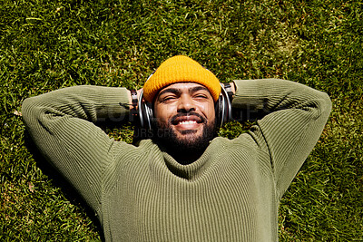 Buy stock photo Relax, music headphones and happy man on grass outdoor, listen to audio online or hearing sound of podcast from top view. Smile, streaming radio and person at park resting for peace, calm and freedom